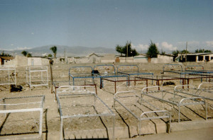 rows of metal bed frames lined up on a dusty street