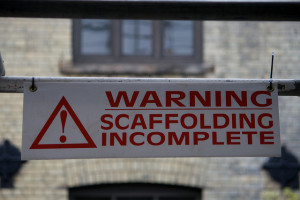 sign in foreground of building reads "scaffolding incomplete"